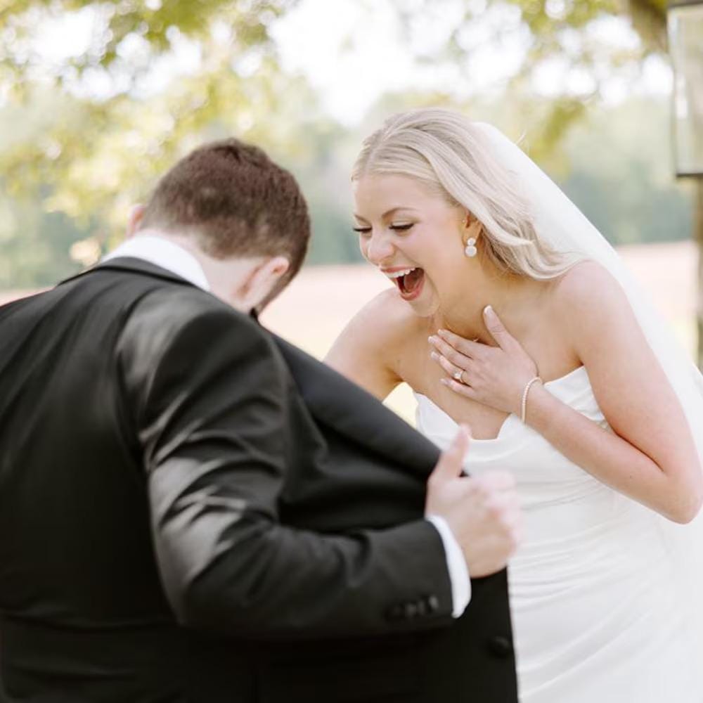 Wedding couple with the bride laughing when looking at the groom inner jacket contain custom photo collage suit lining outdoors with a blurred background