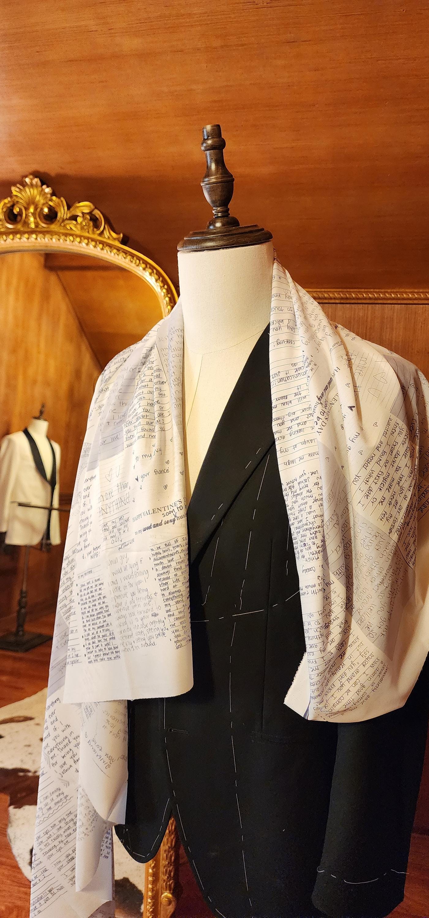 Mannequin wearing a black suit with a custom love notes lining against a wooden wall.