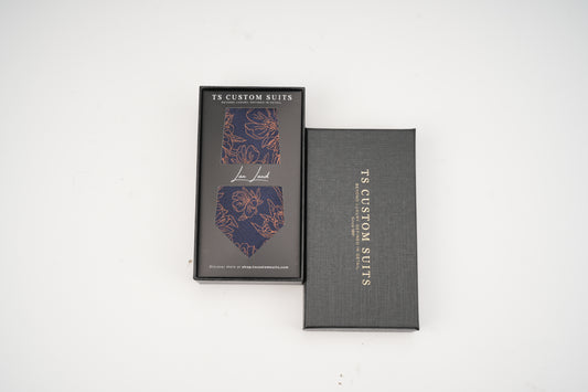 Navy tie with floral pattern in the box with 'TC Custom Suits' branding on a white background