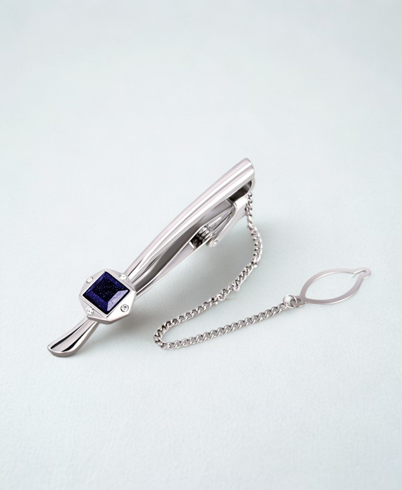 Silver tie clip with a blue gemstone on a light gray background