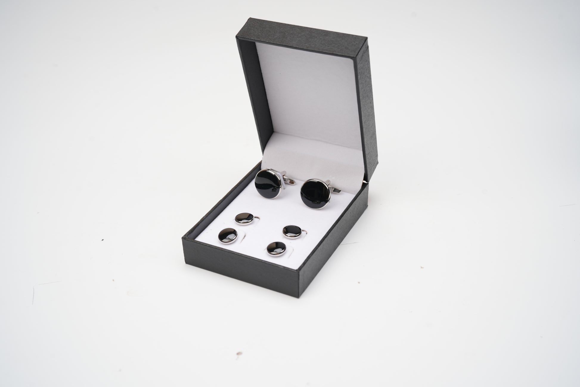 Black cufflinks in an open black box on a white background