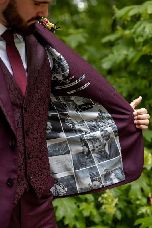 Man wearing a burgundy suit display the custom picture collage suit lining inside jacket against a green leafy background