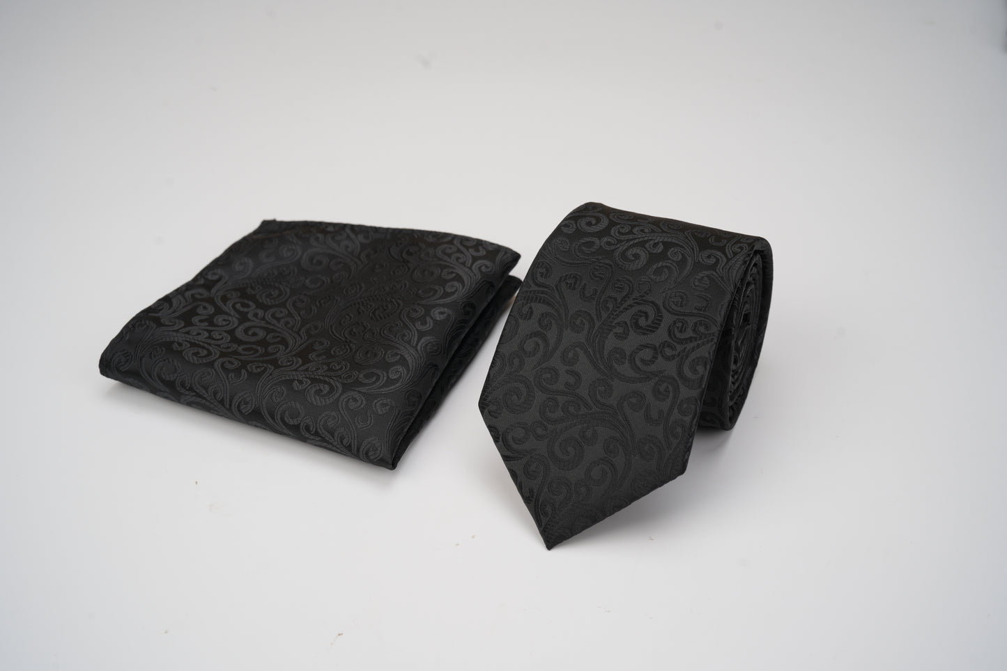 Black patterned tie and pocket square on a white background