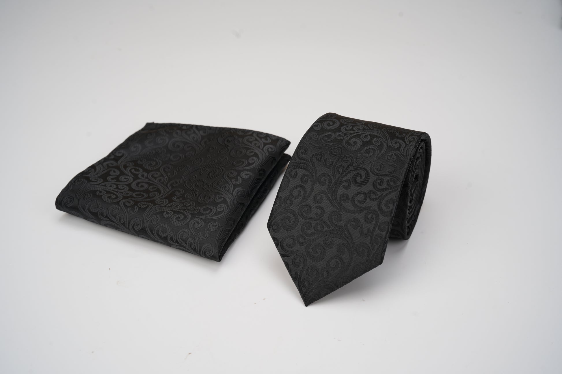 Black patterned tie and pocket square on a white background