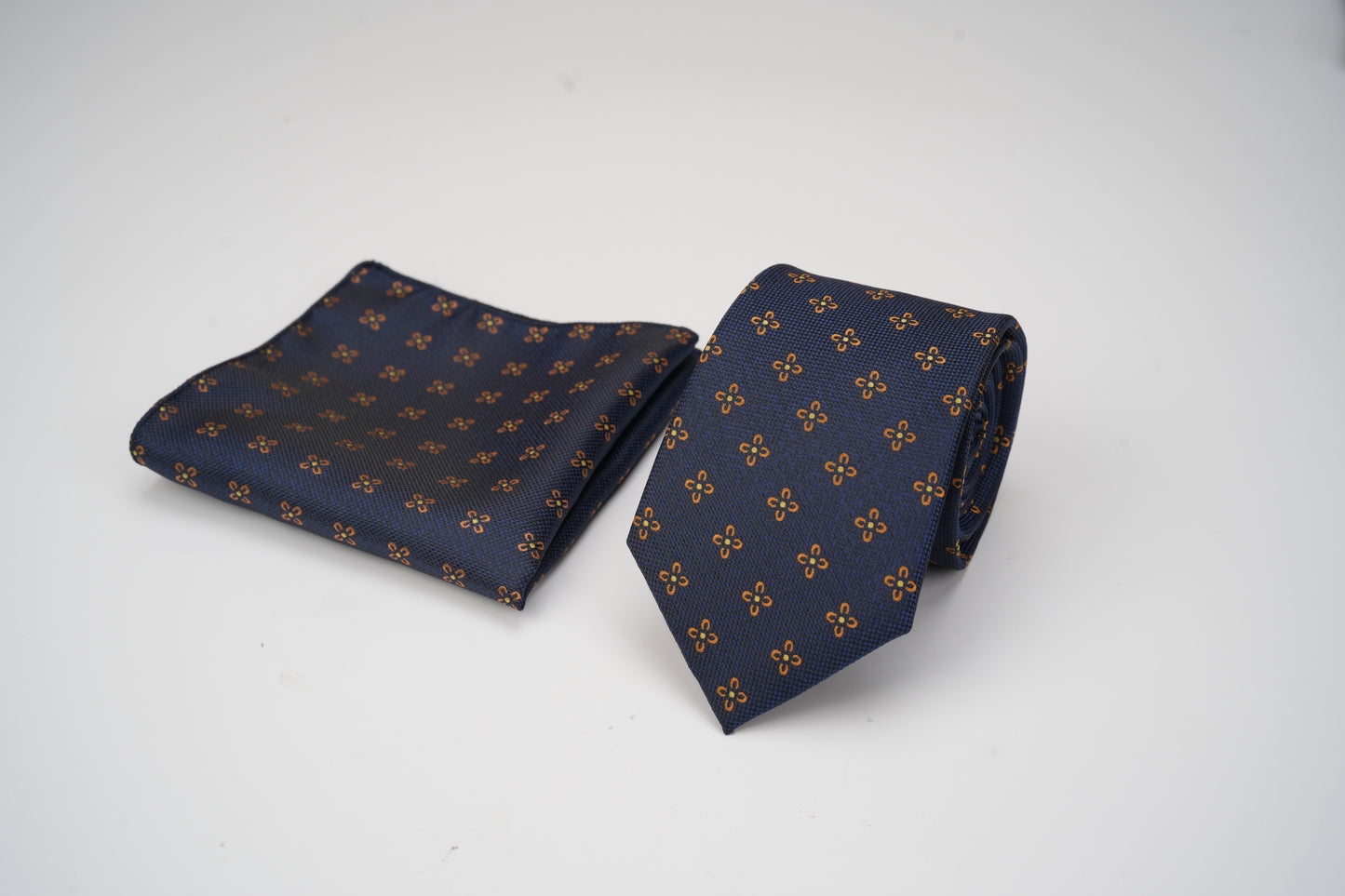 Navy blue tie and pocket square with gold pattern on a white background