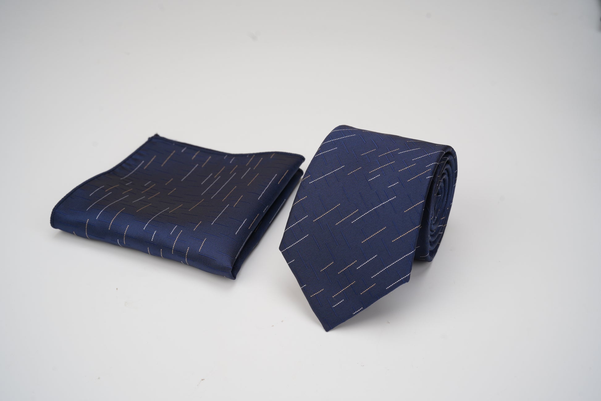 Navy blue tie and matching pocket square with white pattern on a light gray background