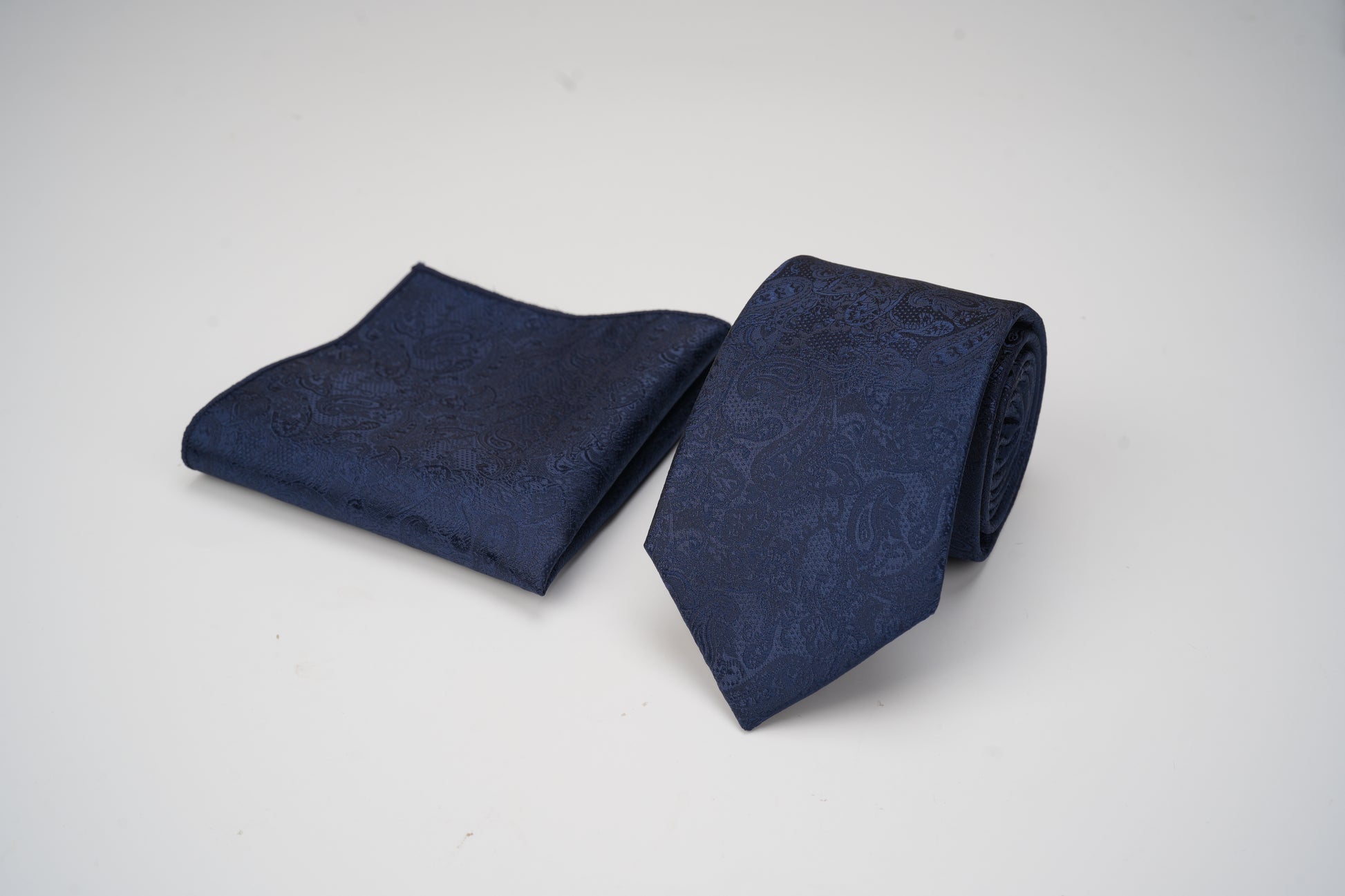 Navy blue patterned tie and pocket square on a light gray background