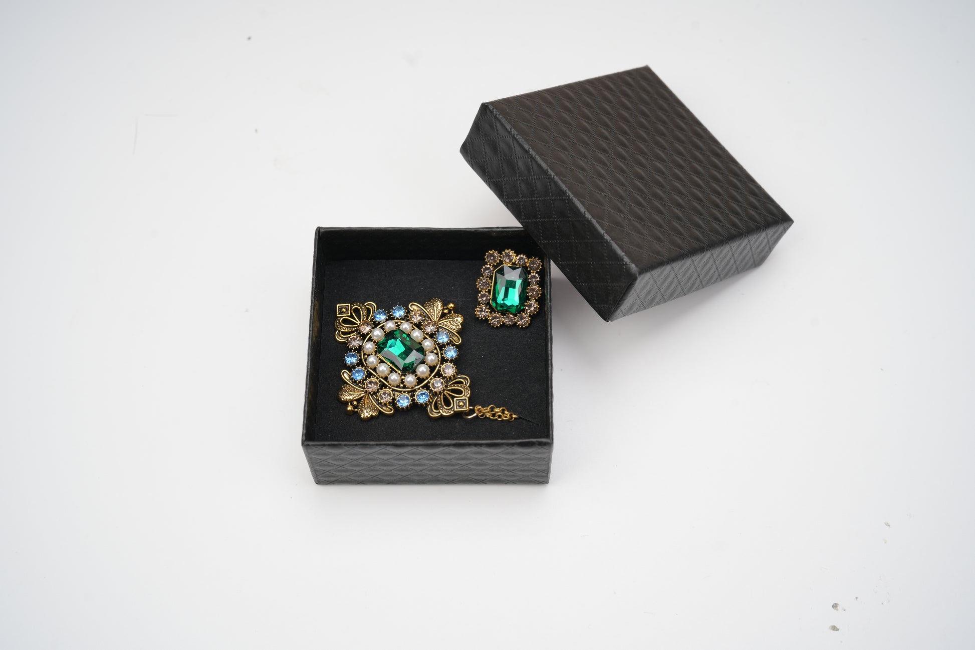 Pair of ornate earrings with gemstones in a black jewelry box on a white background