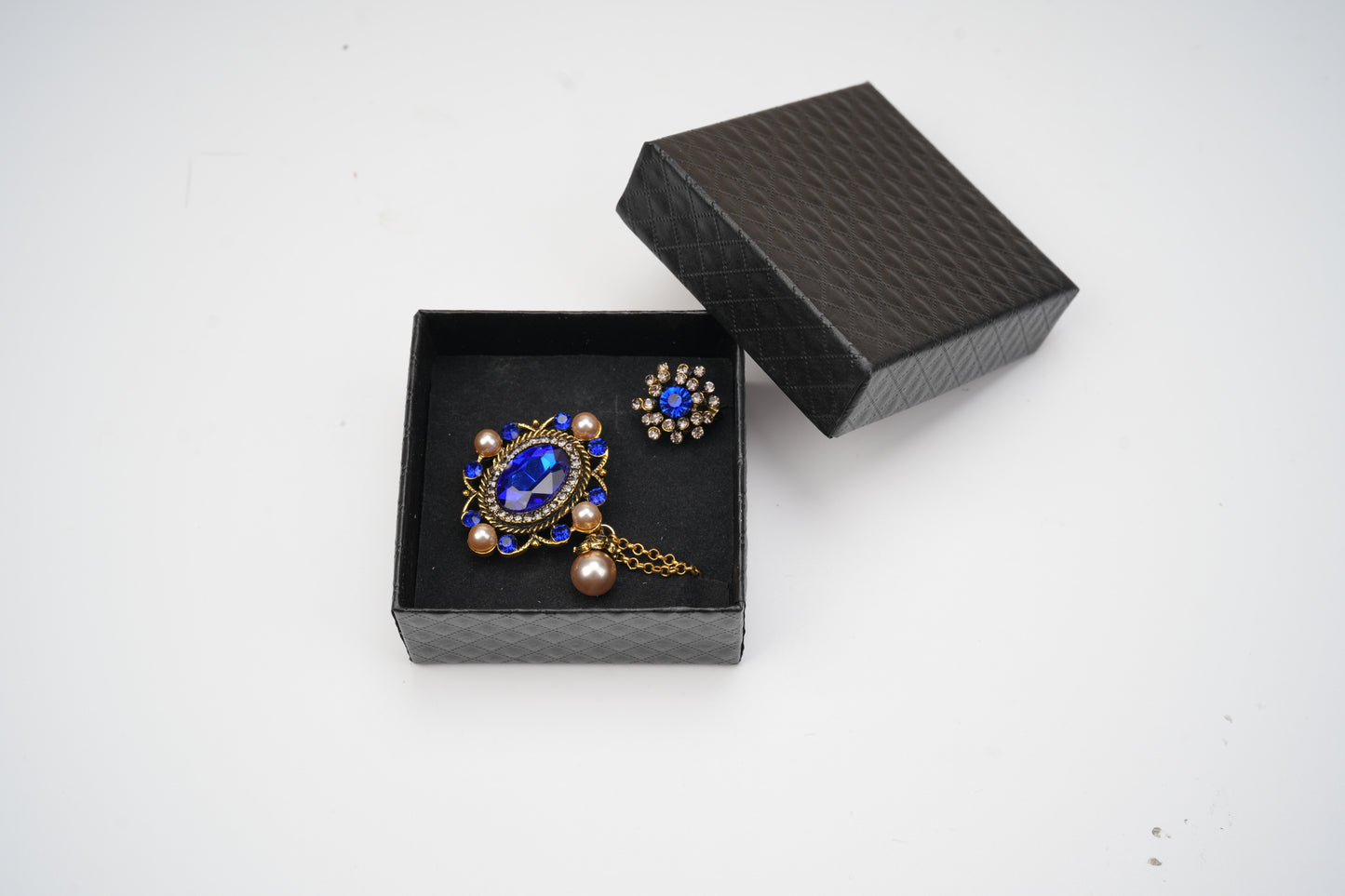 Two decorative brooches in a black jewelry box on a white background