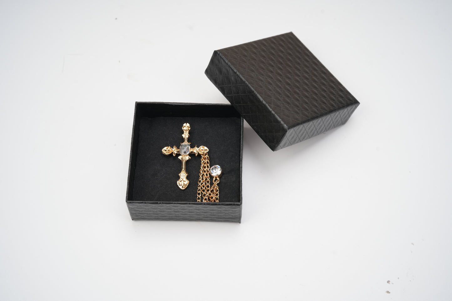 Gold cross pendant in a black jewelry box on a white background