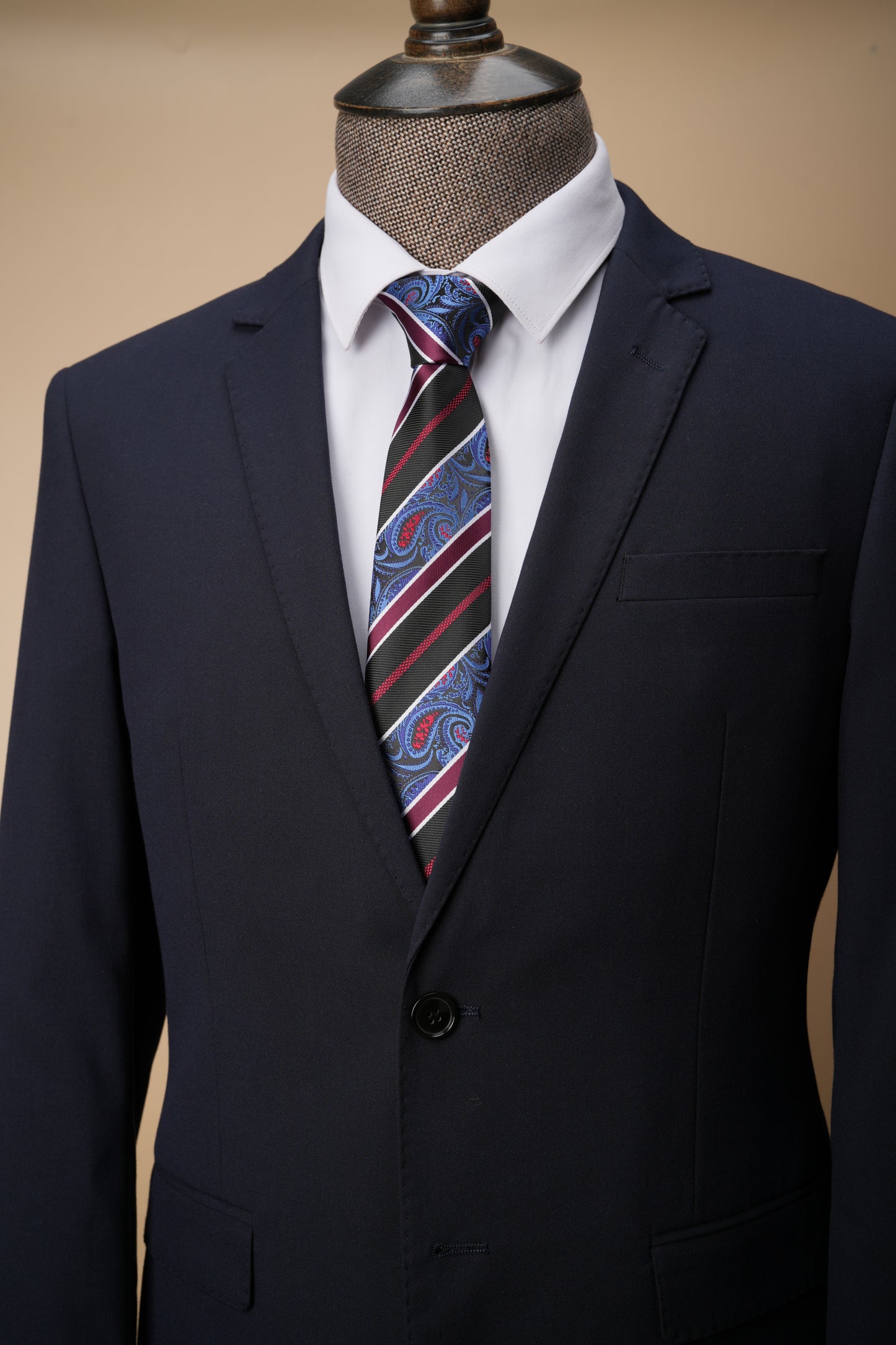 Navy suit with a striped tie on a mannequin against a beige background