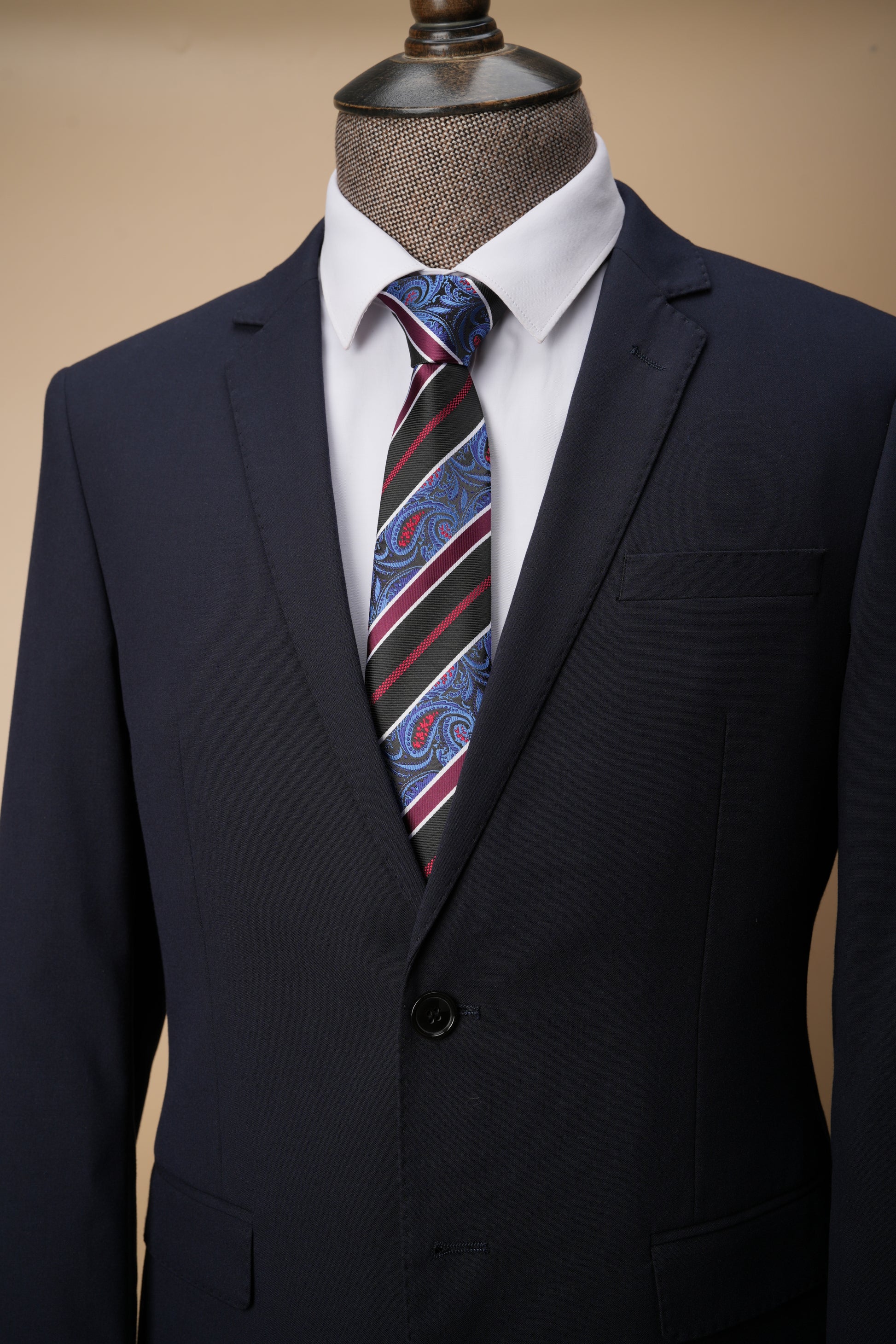 Navy suit with a striped tie on a mannequin against a beige background