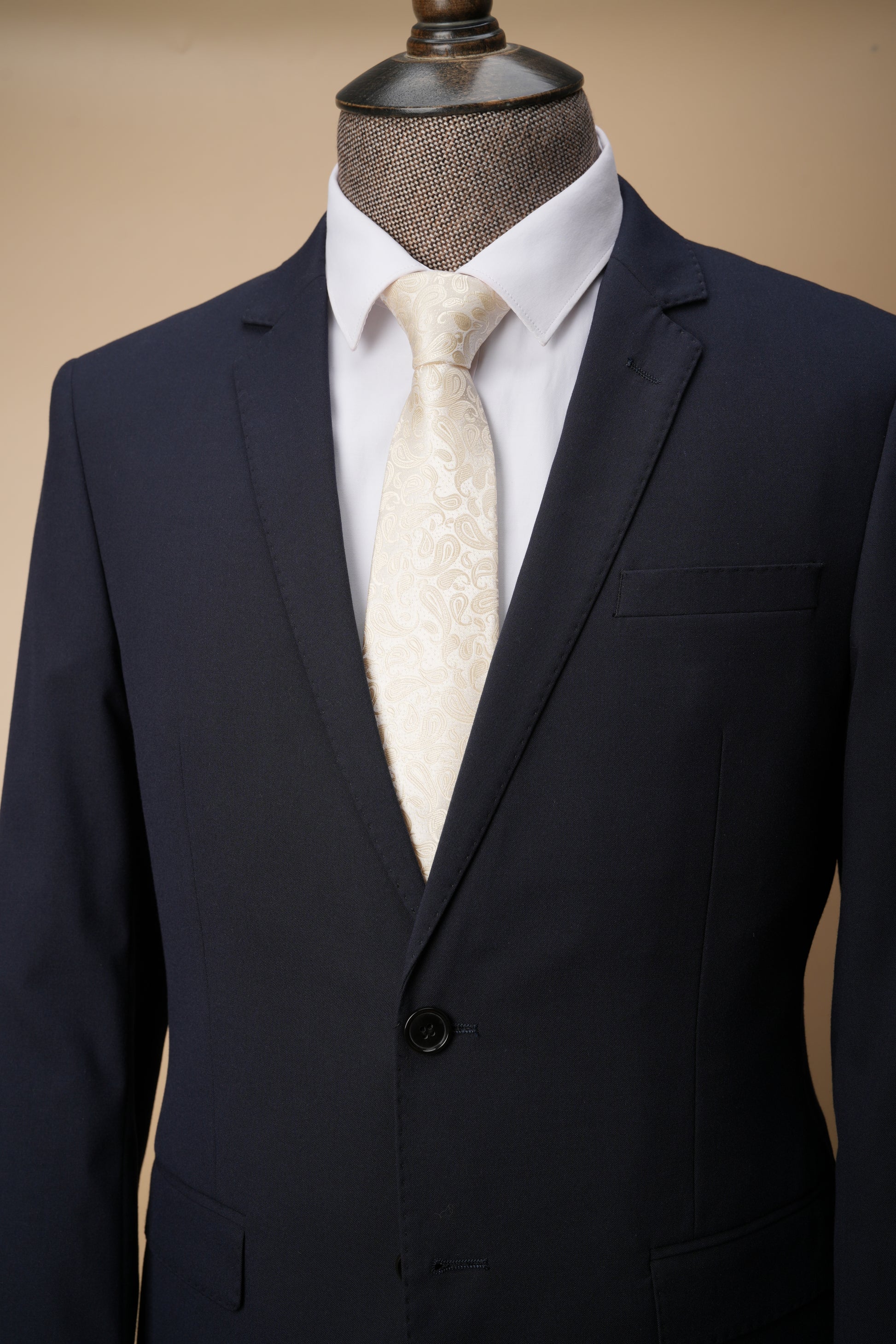 Navy suit jacket with white shirt and patterned tie on a mannequin against a beige background
