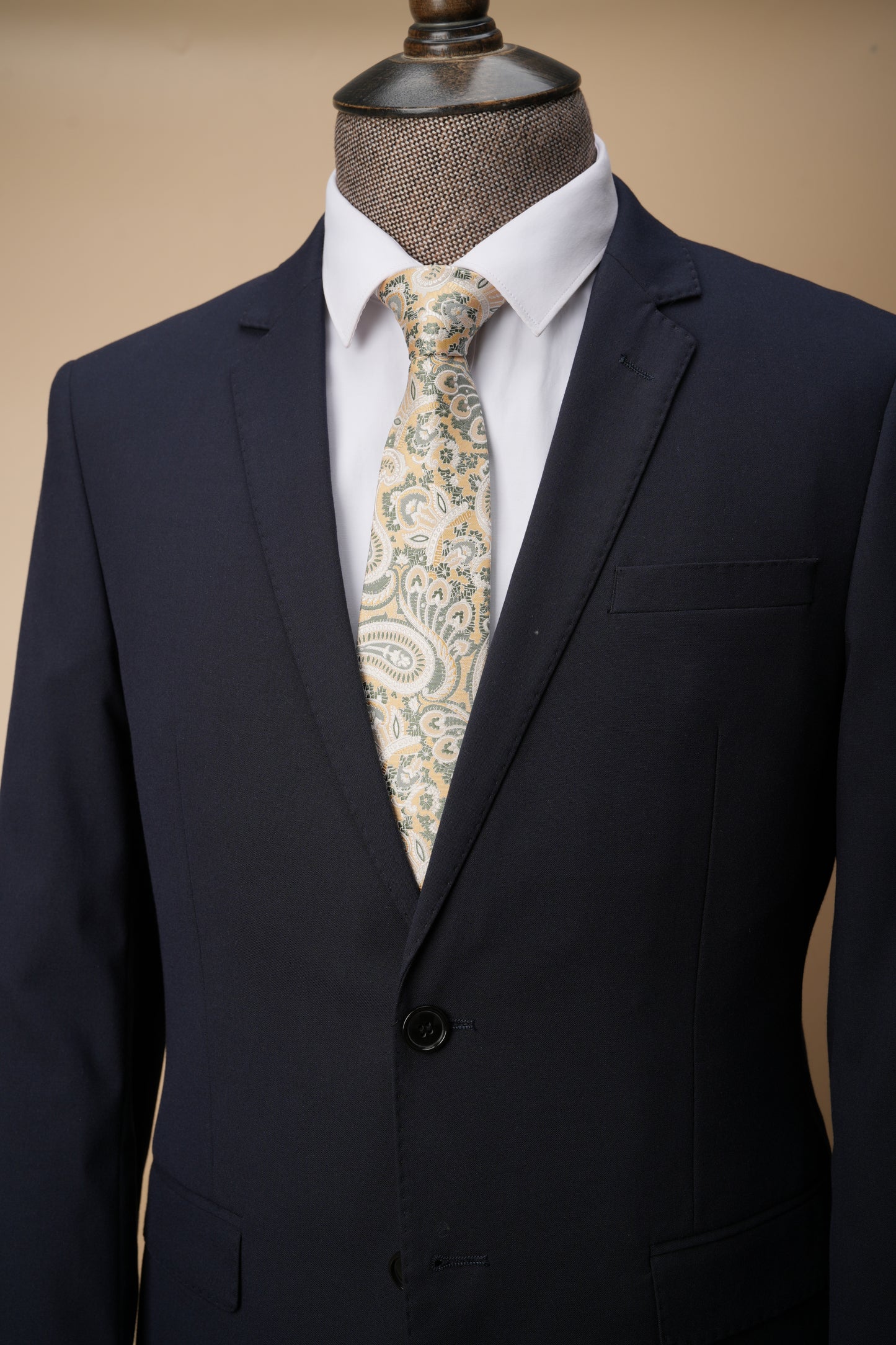 Navy suit jacket with a white shirt and patterned tie on a mannequin against a beige background