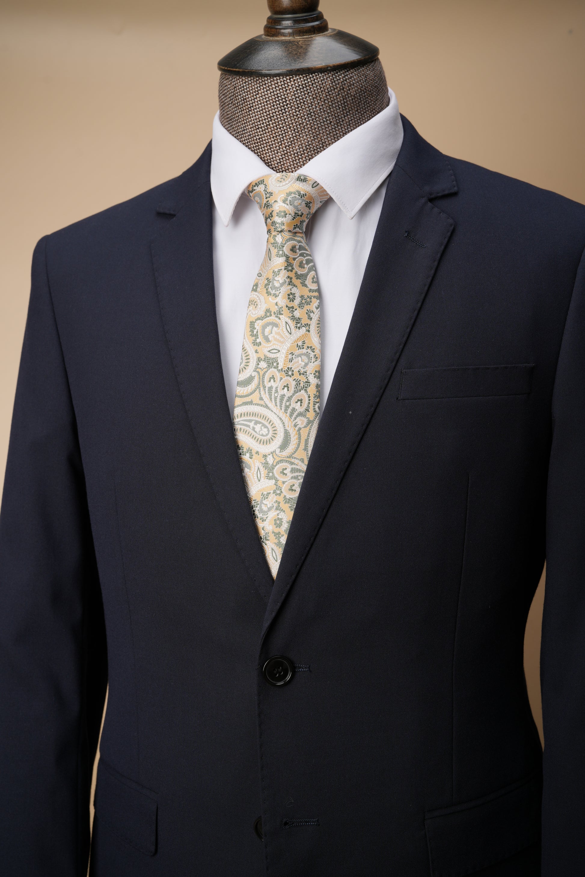 Navy suit jacket with a white shirt and patterned tie on a mannequin against a beige background