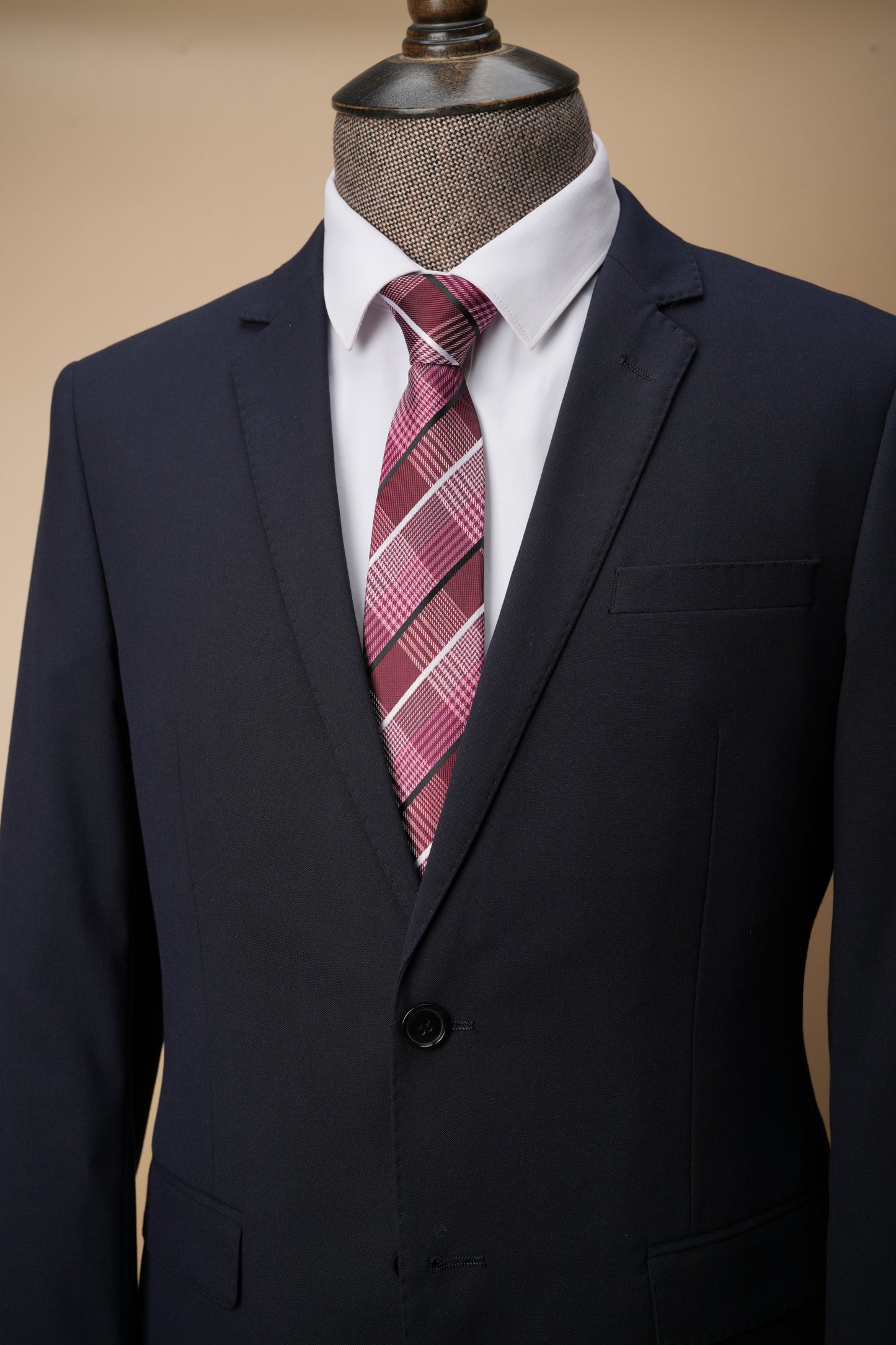 Navy suit with a white shirt and red plaid tie on a mannequin against a beige background