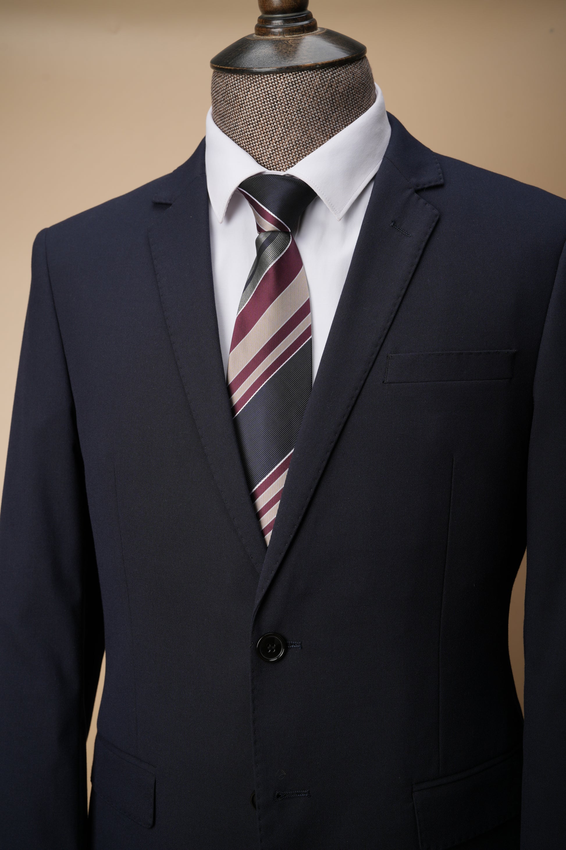 Navy suit jacket with a striped tie on a mannequin against a beige background