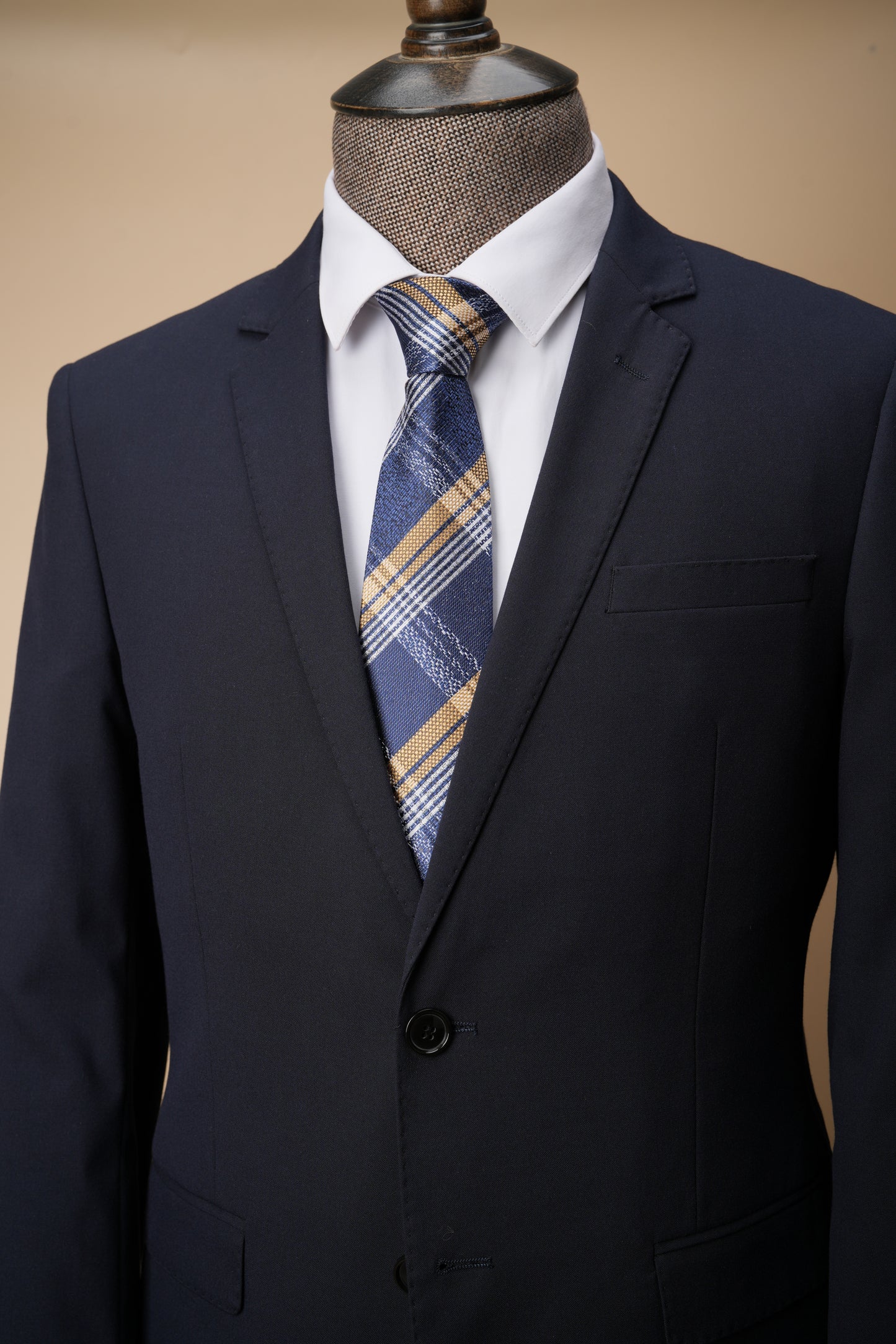 Navy suit jacket with a plaid tie on a mannequin against a beige background