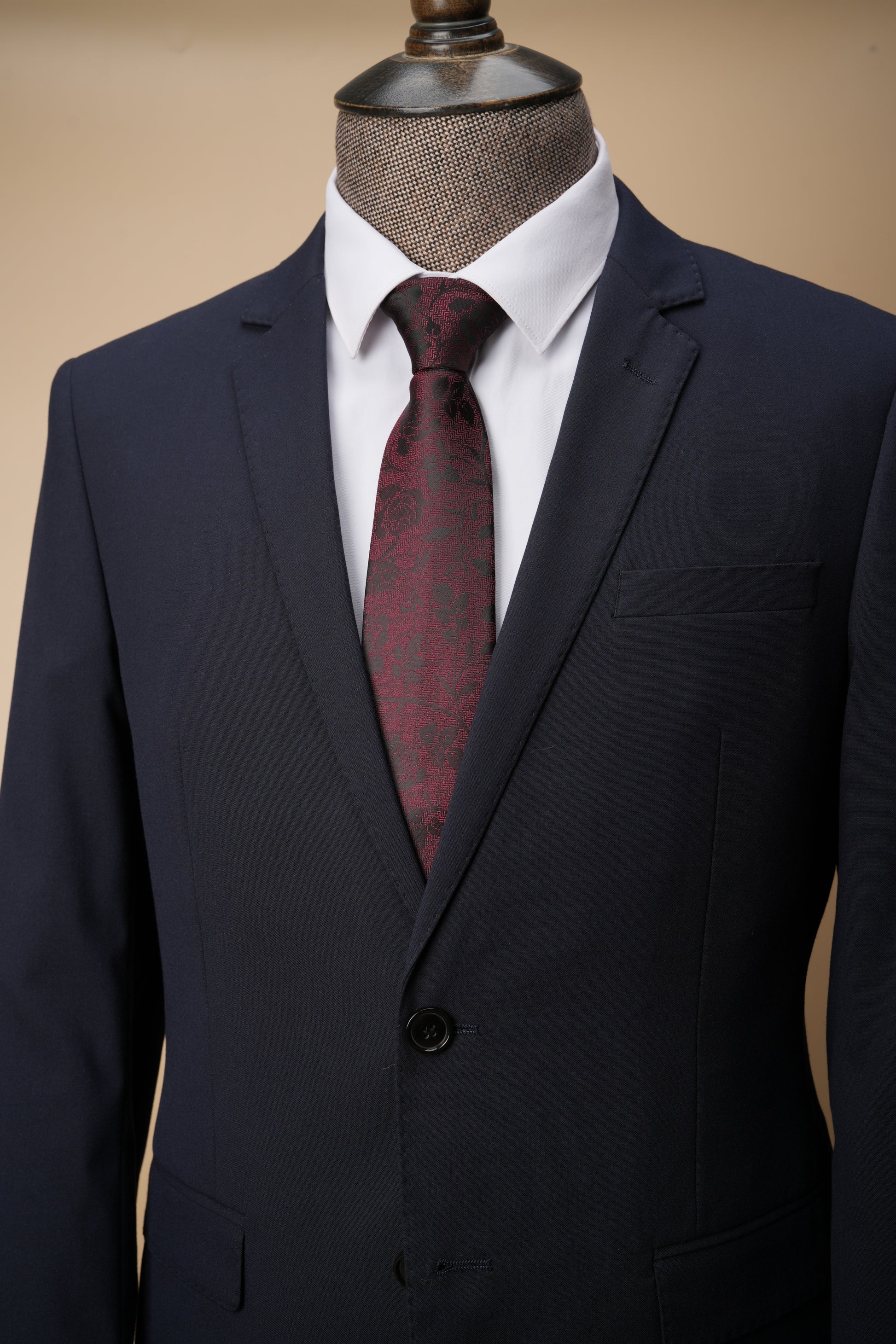 Navy suit jacket with a white shirt and red tie on a mannequin against a beige background
