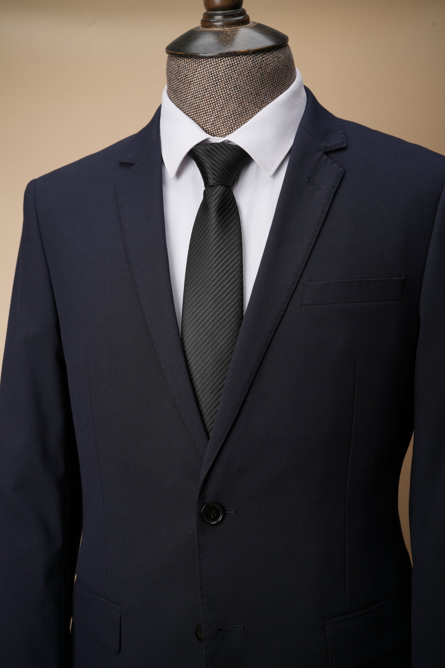 Black suit jacket with a white shirt and black tie on a mannequin against a beige background
