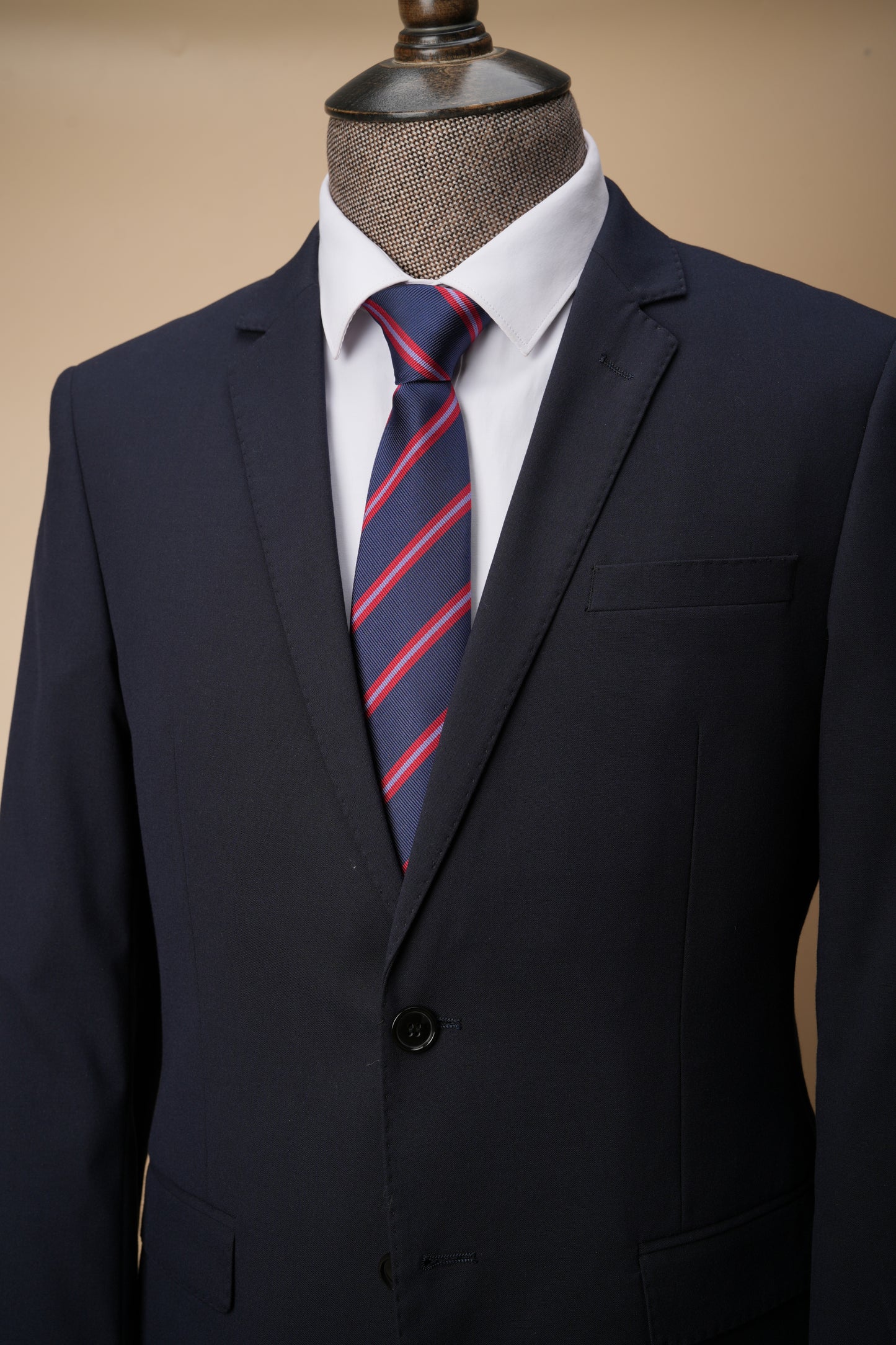 Navy suit with a red and blue striped tie on a mannequin against a beige background