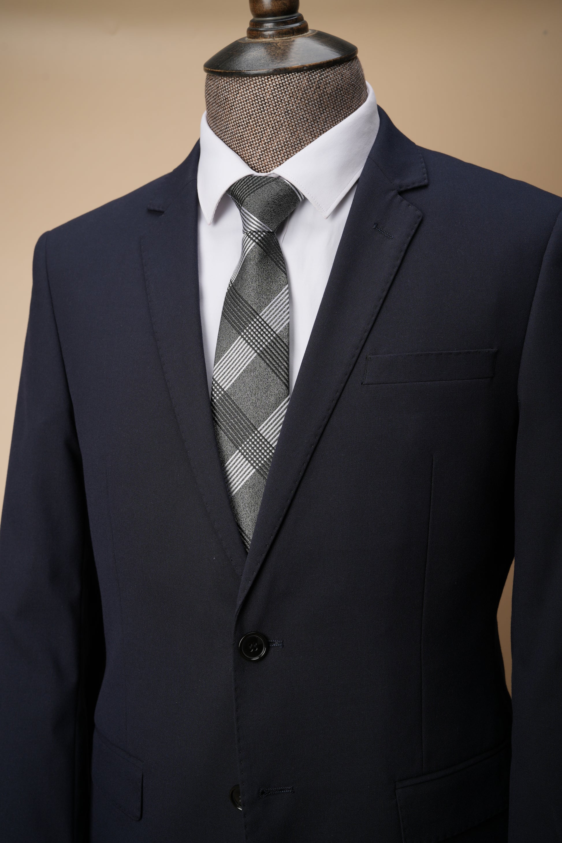 Navy suit jacket with a plaid tie on a mannequin against a beige background
