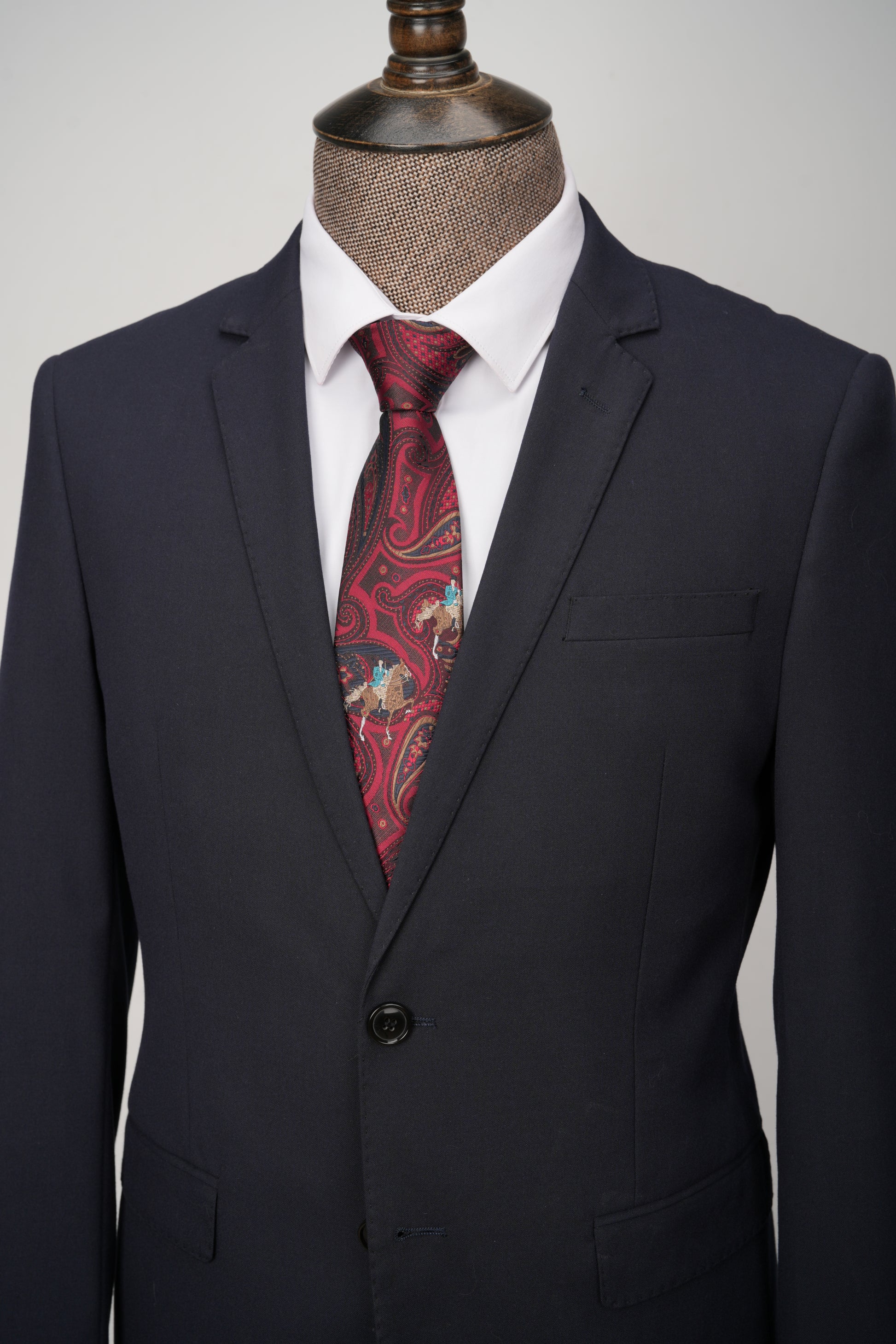 Black suit jacket with a red paisley tie on a mannequin against a gray background