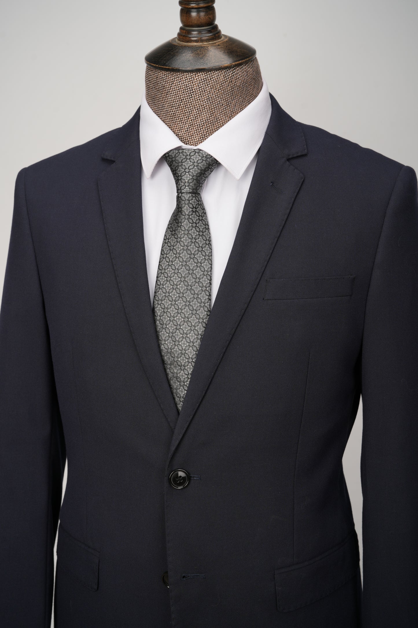 Black suit jacket with a white shirt and patterned tie on a mannequin against a gray background