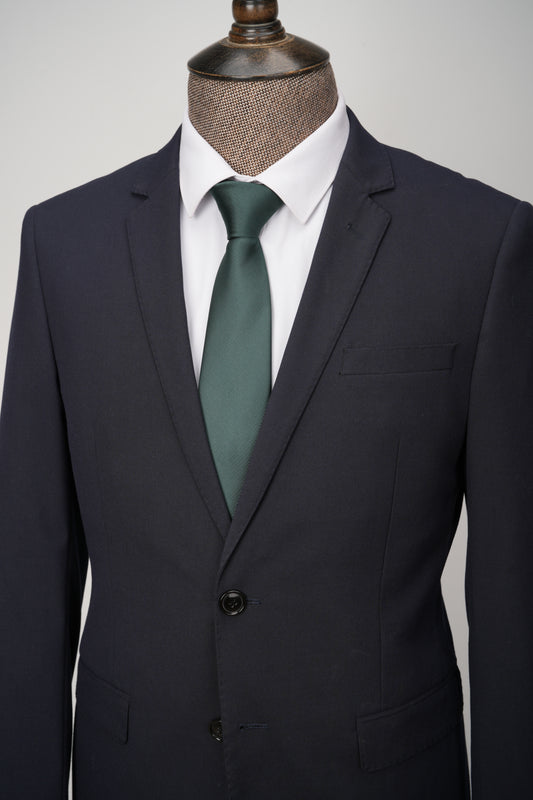 Dark suit with a green tie on a mannequin against a gray background