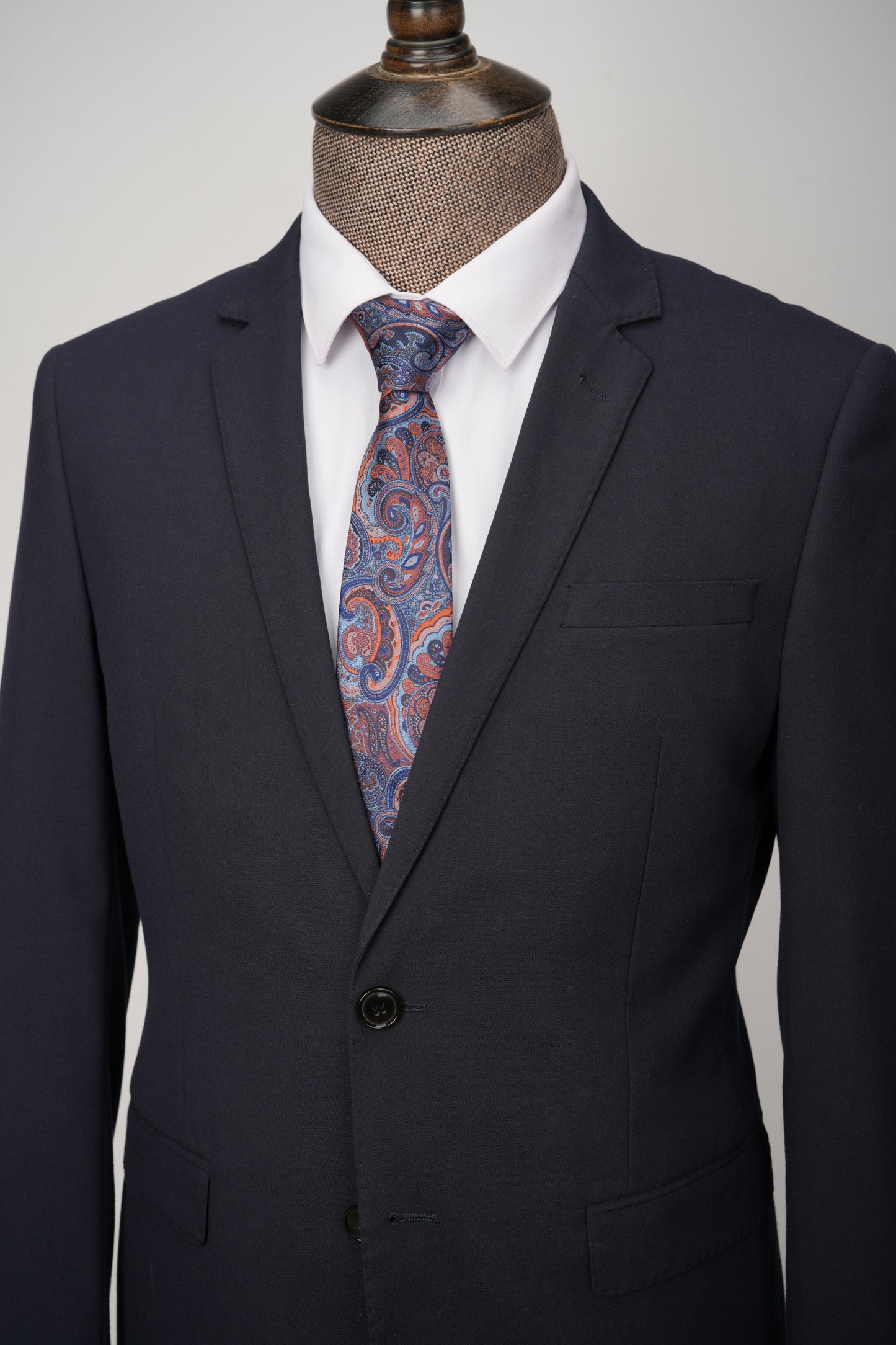 Dark suit jacket with a white shirt and patterned tie on a mannequin against a gray background