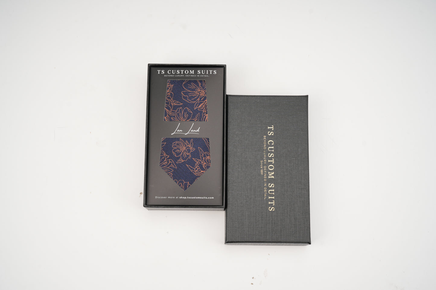 Navy tie with floral pattern in the box with 'TC Custom Suits' branding on a white background