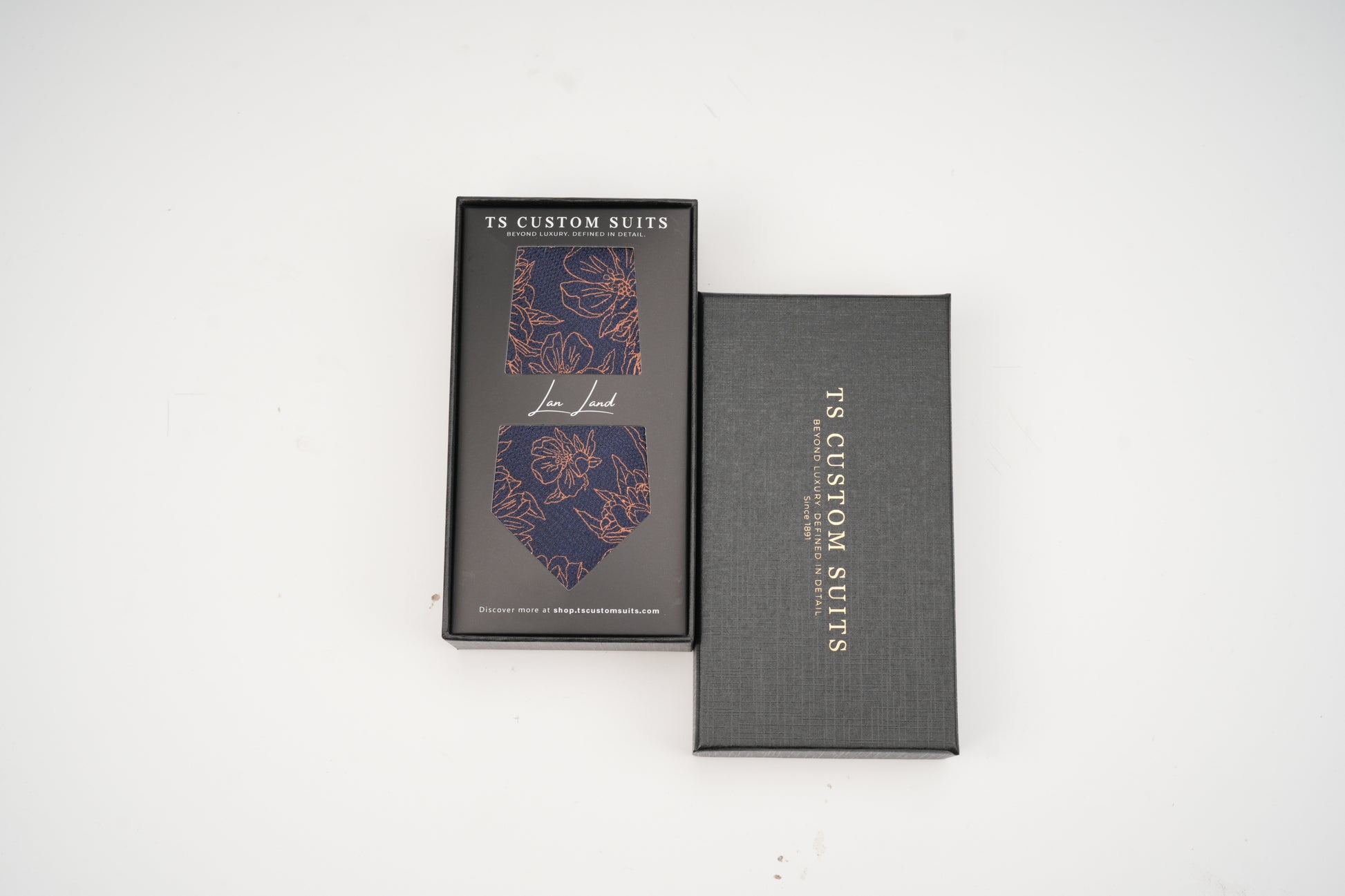 Navy tie with floral pattern in the box with 'TC Custom Suits' branding on a white background