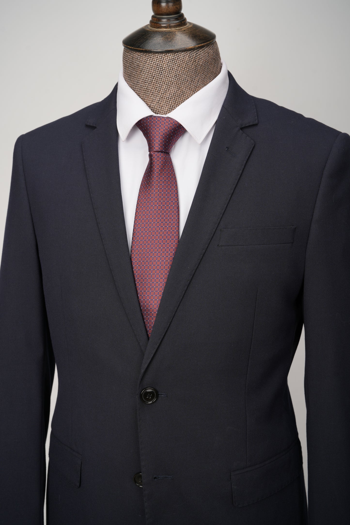 Dark gray suit with a red patterned tie on a mannequin against a light gray background