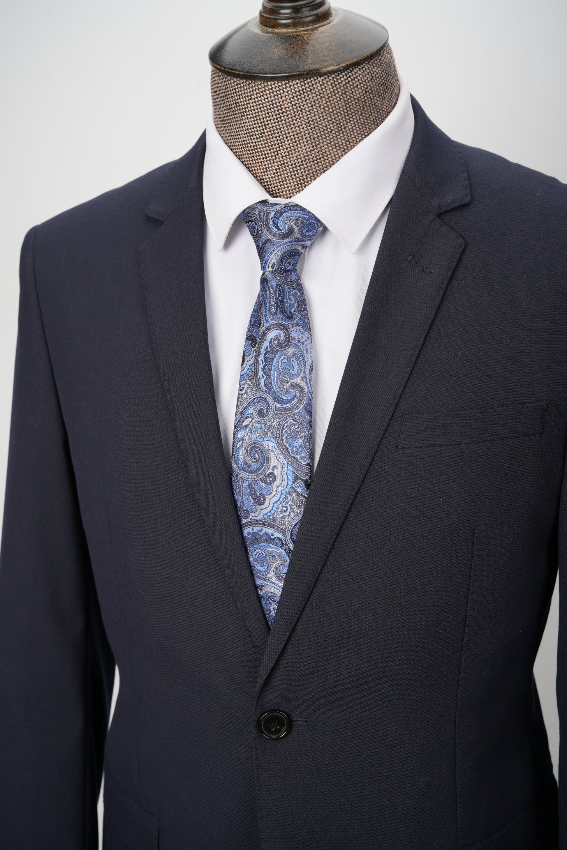 Navy suit with a white shirt and blue paisley tie on a mannequin against a white background