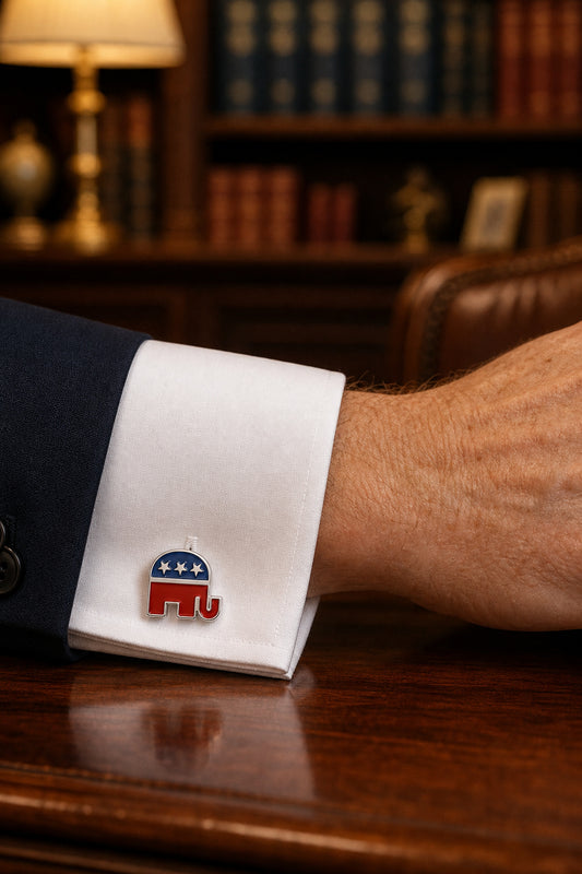 A white dress shirt cuff with a red and blue elephant cufflink, worn on a man's wrist in a warm, book-filled office setting.