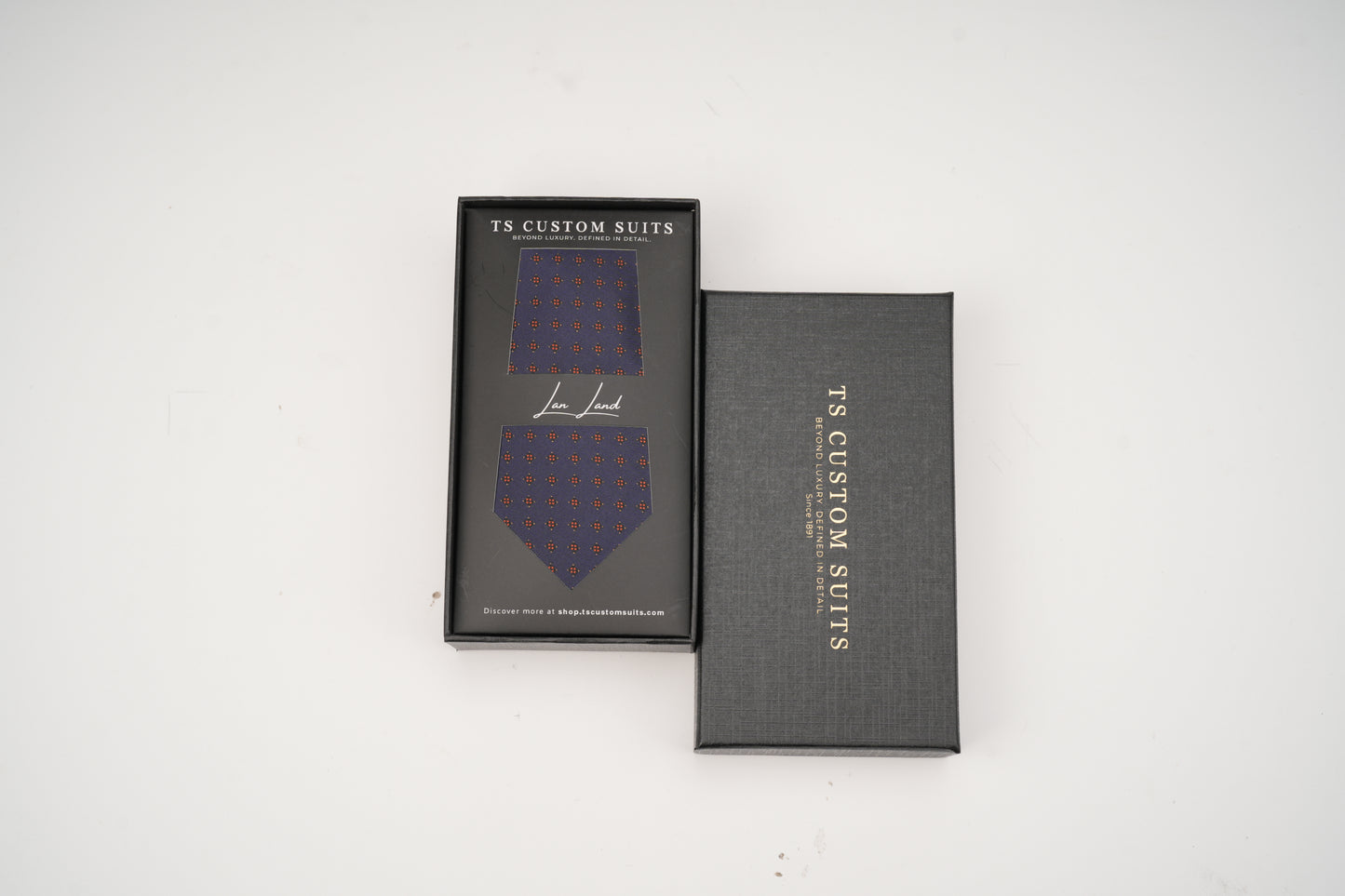 Blue patterned tie in a black box with 'TS Custom Suits' branding on a white background