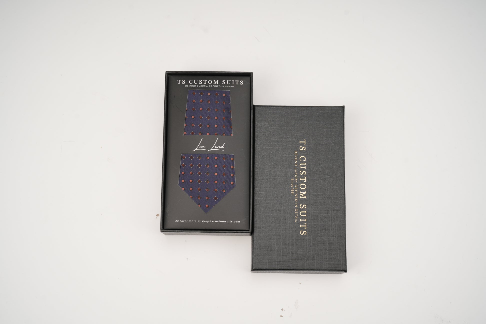 Blue patterned tie in a black box with 'TS Custom Suits' branding on a white background