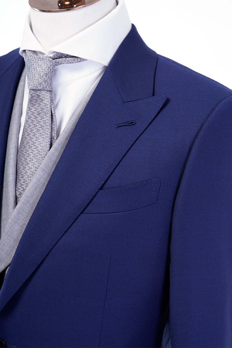 Blue wedding suit with peak lapel, a double breasted grey vest and grey pants. Blue and grey wedding suit. Blue wedding suit for groom. Grey wedding suit for groom. Blue suit with ticket pocket. Double breasted vest with shawl lapel.