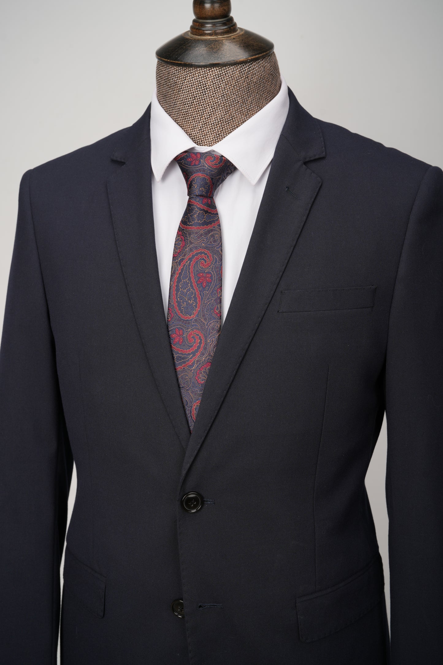 Black suit with a red paisley tie on a mannequin against a gray background