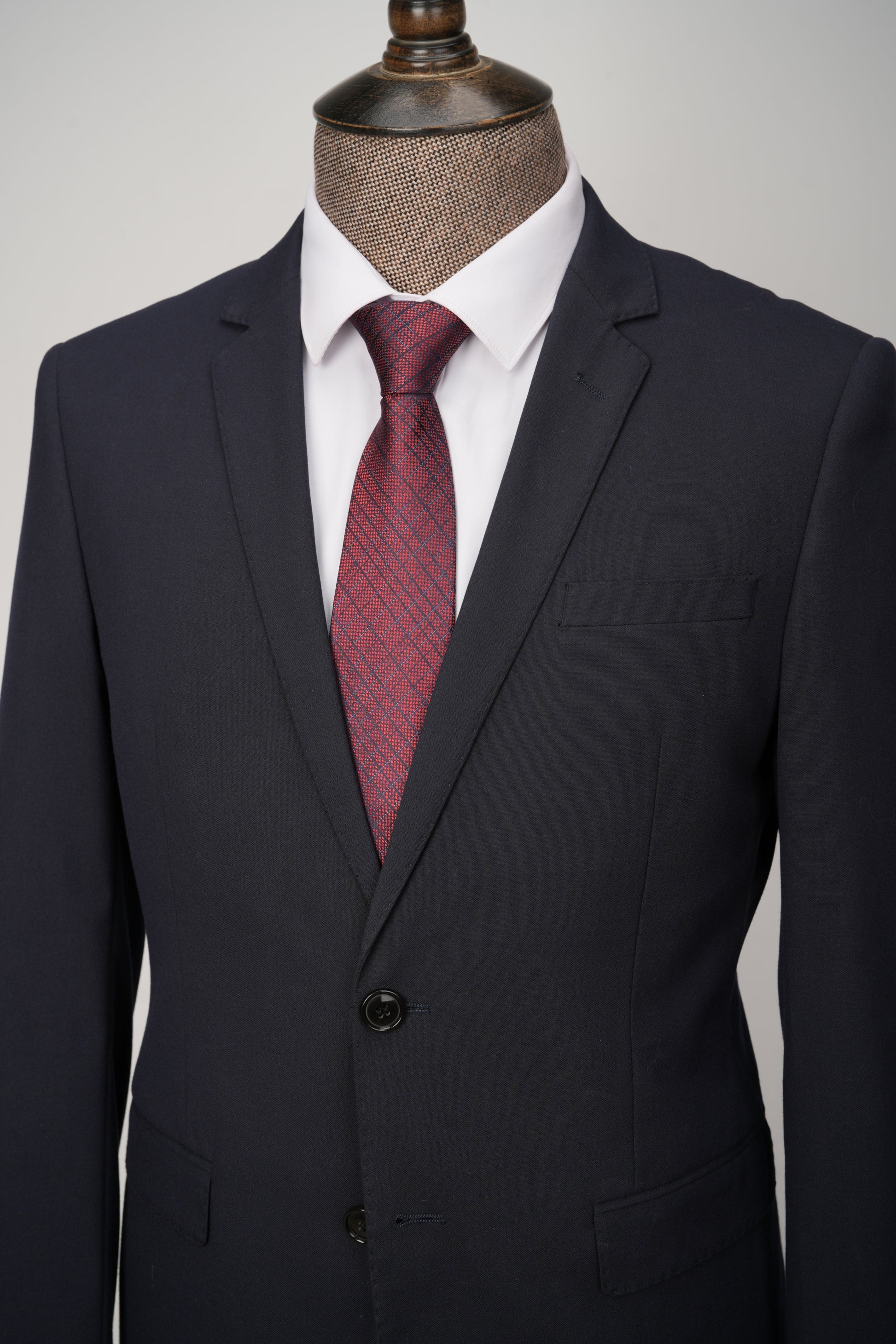 Black suit jacket with a red patterned tie on a mannequin against a gray background